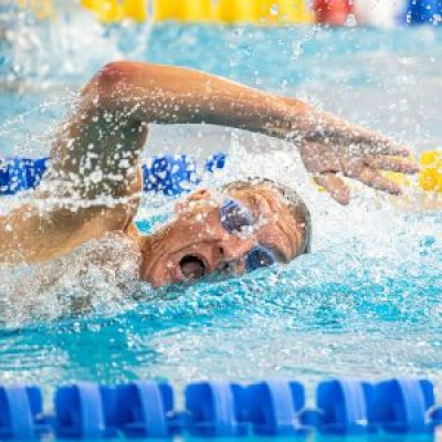 A National Senior Games athlete wearing goggles mid-stroke during a freestyle swimming race.